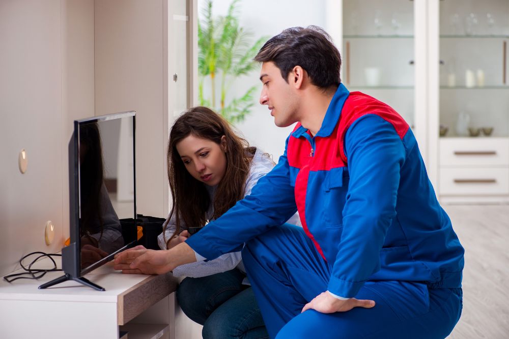 A man and woman in blue overalls assess a television, showcasing appliance repair services available in Everett, WA.