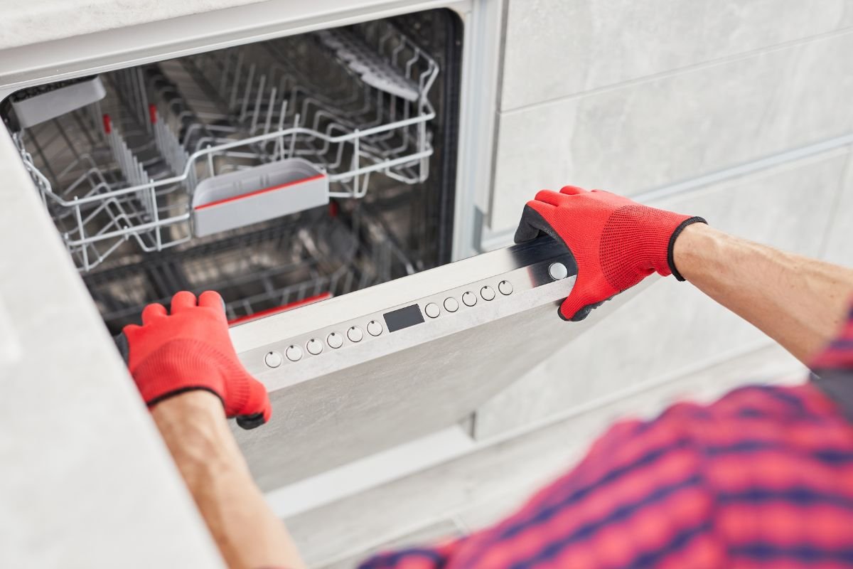A man wearing red gloves is carefully holding a dishwasher, preparing for installation or maintenance.