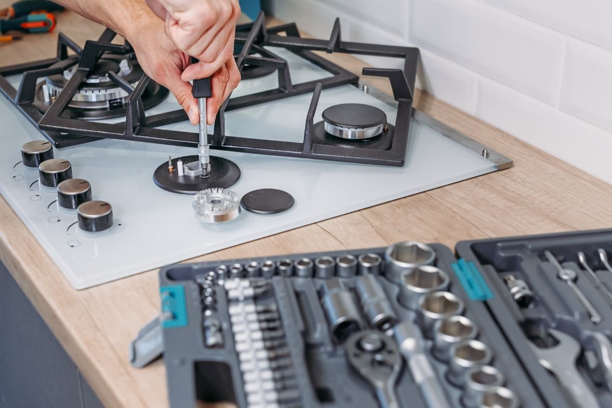 A man repairs a stove top using various tools, demonstrating his skills in home maintenance.