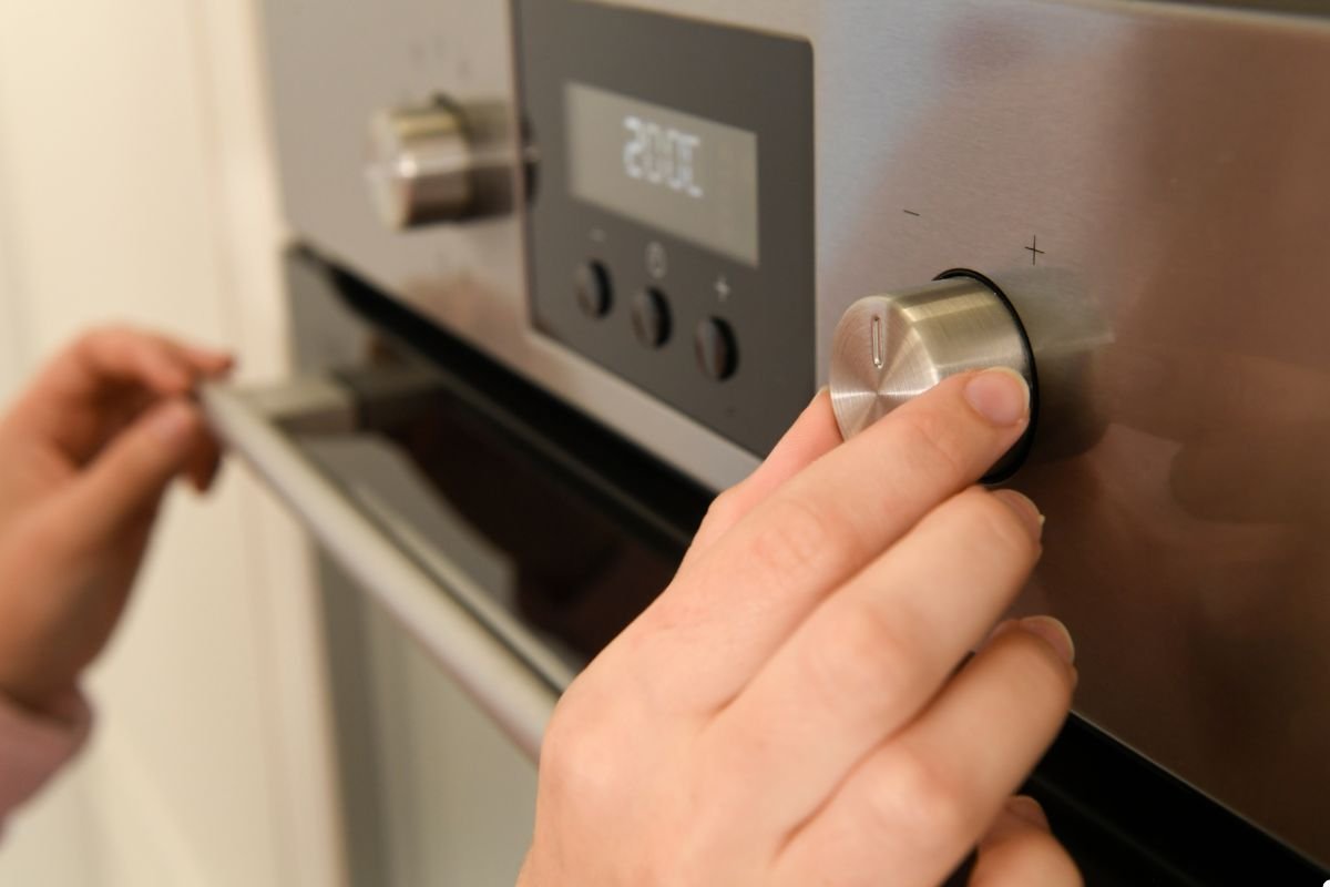 A person carefully adjusts the oven knob on a stove, preparing to cook a meal.